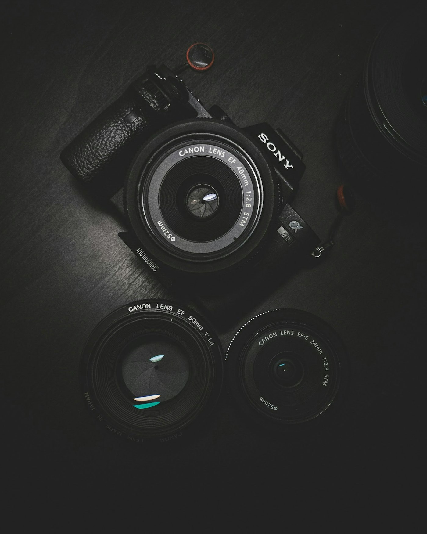 A moody flat-lay of a camera body and prime lenses arranged on a black surface