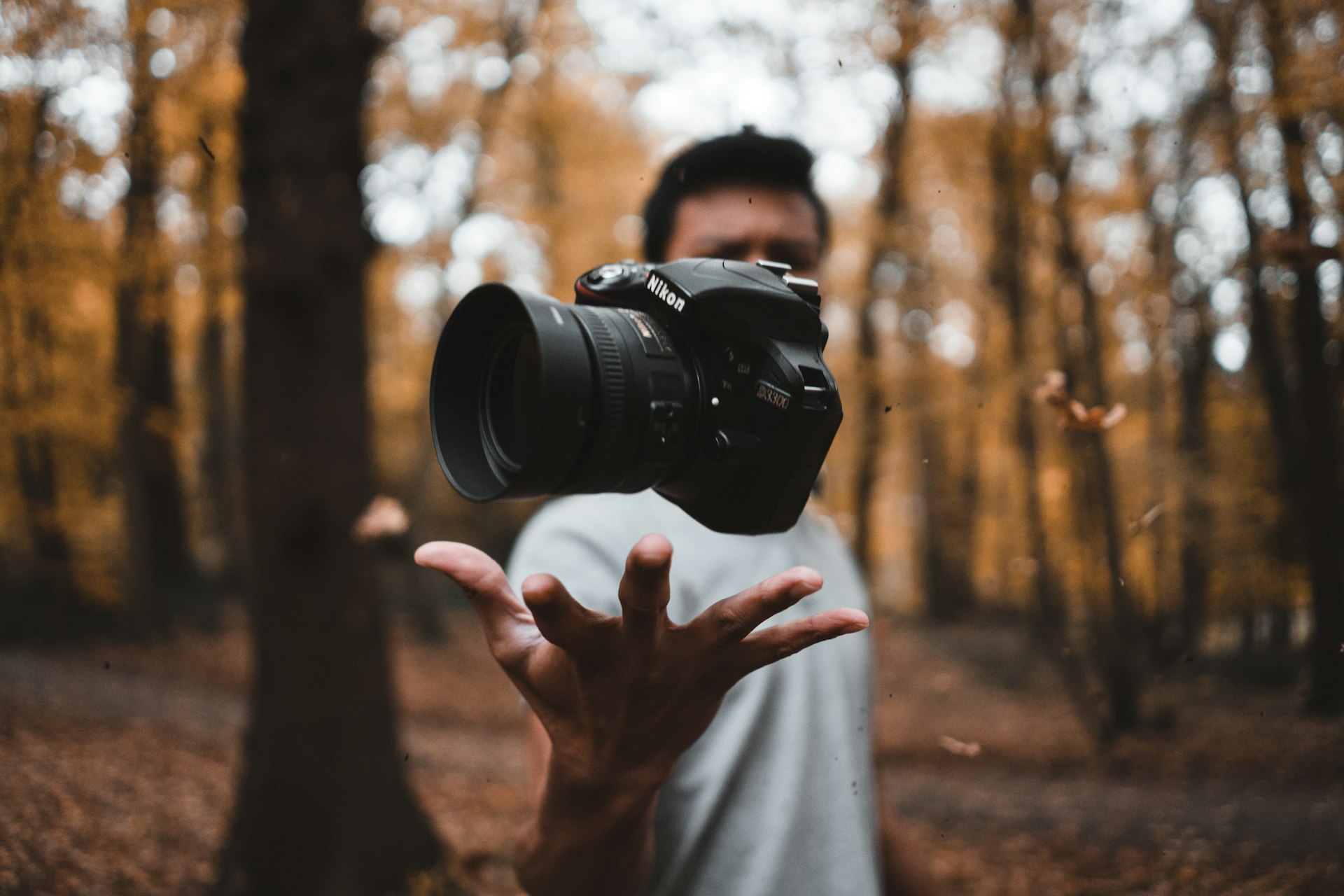 A photographer tossing and catching a Nikon DSLR amid warm golden bokeh in an autumn forest