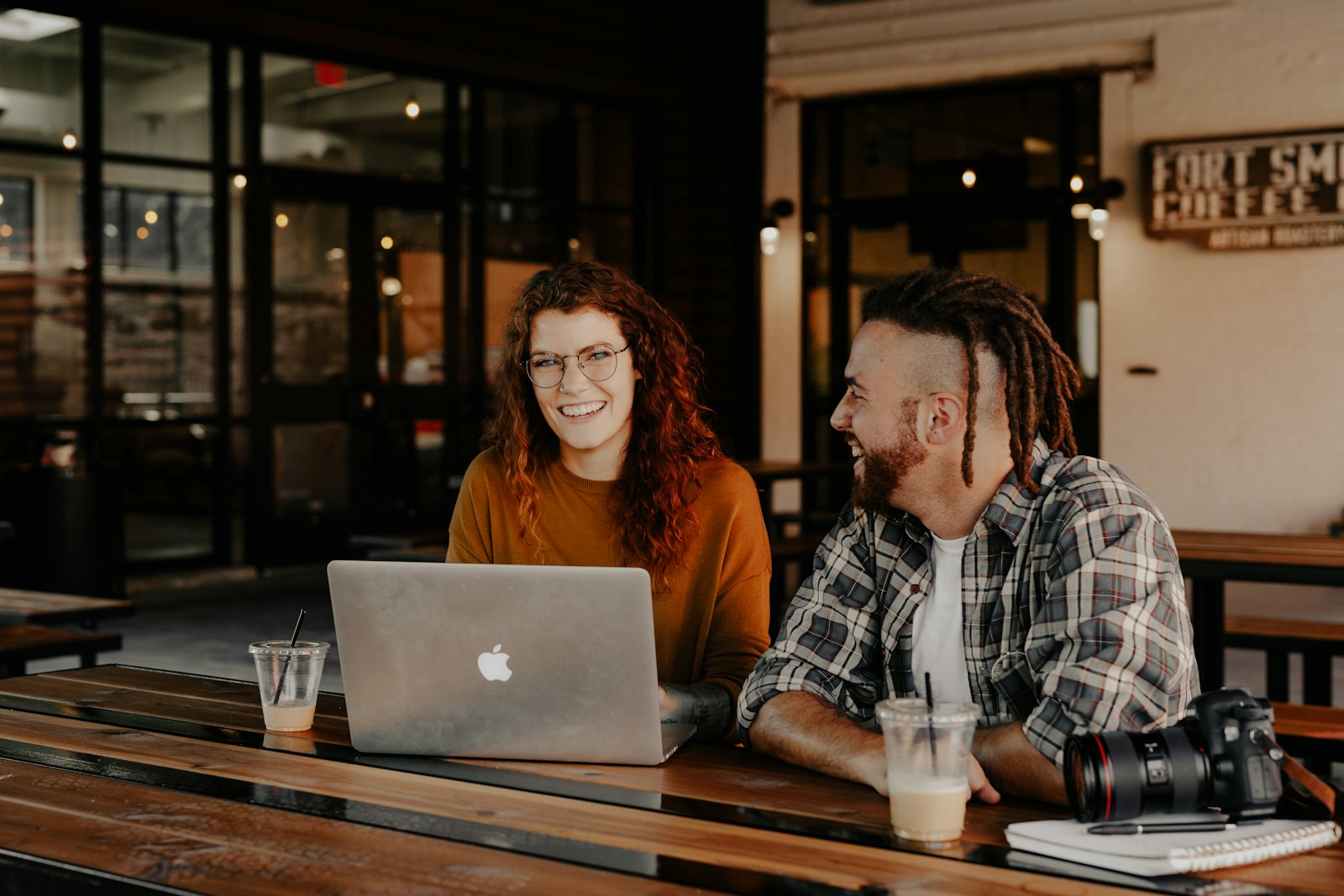 Two creatives reviewing photo work together on a laptop in a warm cafe